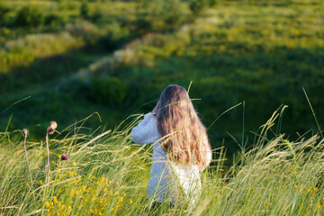    Happy cute smiling caucasian girl walking on the meadow and picking a bouquet of wildflowers.  Summer sunset.  Happy Childhood concept. Nature background. Copy space