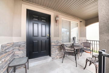 Front porch of a house with black door and a stone bricks wall siding
