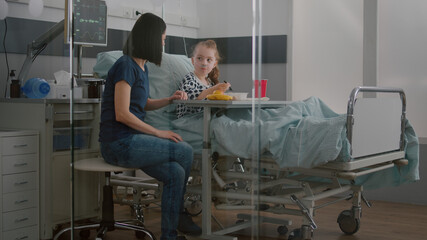 Sick child patient sitting in bed with oxygen nasal tube eating healthy food during lunch in...