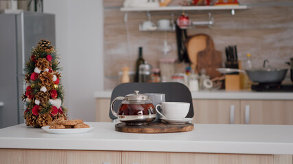Empty xmas decorated culinary kitchen with nobody in it ready for christmas holiday. On table standing baked homemade delicious cookie and cup of coffee waiting for traditional morning dessert