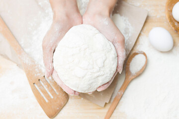 Raw yeast dough in your hands on a floured kitchen table, the idea of a recipe. The concept of home baking or making dough.