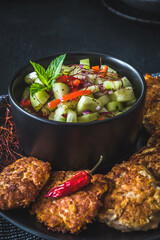 Fresh cucumber salad in a black bowl with fish or vegetable patties or meatballs around, vertical