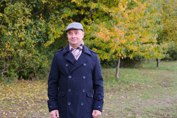 elderly crazy man in a coat walks in an autumn park against a background of trees, the concept of a healthy lifestyle, good mood, happiness at any age