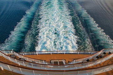 Looking down at the aft or back decks of a cruise ship and the wake or waves in the sea as it sails...