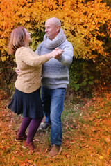 aged man and woman have fun dancing in the autumn park against the background of trees, the concept...