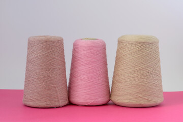Pastel color bobbins of wool yarn for hand and machine knitting on a pink background