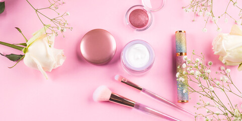 Trendy make up brushes with products on pink background with gypsophila flowers