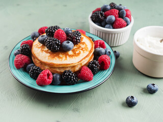 Stack of pancakes with raspberries and blueberries served in a dish on green background