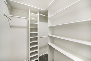 Small empty walk in closet with white interior and built in shelving units