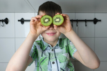 child, kid 8-10, boy sitting in the kitchen at home, juicy cut green kiwi instead of eyes, head...