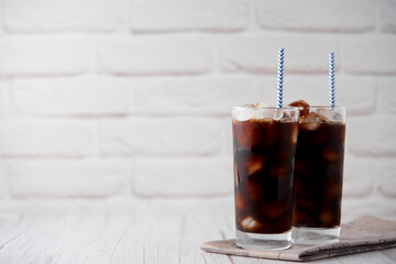 Iced coffee in a tall glass with straws on a white wood background. Cold tasty summer refreshment...