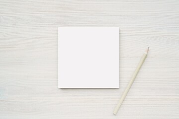Square notepad mockup, white empty paper card and pencil on white wood background, top view,...