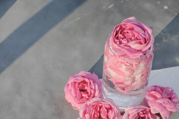 Cold cocktail of pink tea rose petals in a glass glass on a gray background with rose flowers
