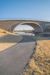 Concrete trail in the middle of a grass with a view of an arched bridge