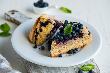 Sliced blueberry sponge cake on a white plate on a light concrete background. Baking berries.