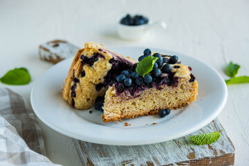 Sliced blueberry sponge cake on a white plate on a light concrete background. Baking berries.