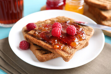 Tasty toast with raspberry jam and fresh berries for breakfast on table, closeup