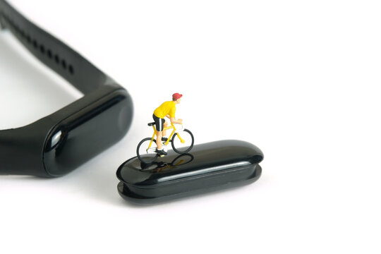 Miniature people toy figure photography. Bike cycling trainer and tracing health app. A biker cycling above smartwatch, isolated on white background.