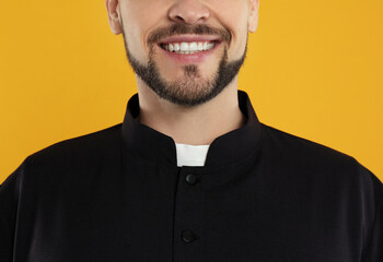 Priest wearing cassock with clerical collar on yellow background, closeup - obrazy, fototapety, plakaty