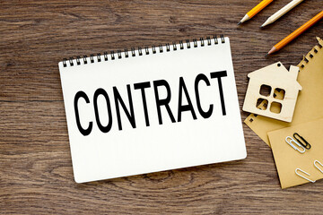 Contract Papers on wooden desk, text on a wooden table, on white paper near the figure of a house made of wood