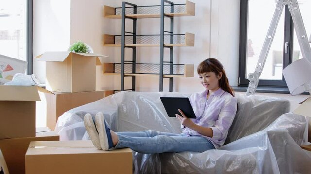 moving, people and real estate concept - happy smiling asian woman with tablet pc computer and boxes at new home