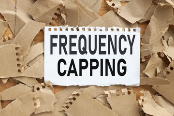 FREQUENCY CAPPING, text on white paper on torn kraft paper background