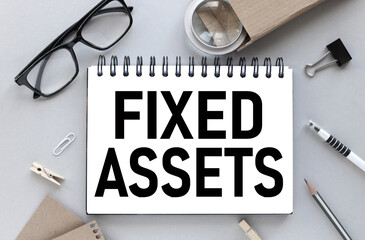 Fixed Assets . text on white paper on gray background near magnifier and glasses