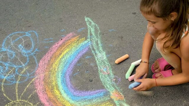 The child draws a rainbow with chalk. Selective focus.