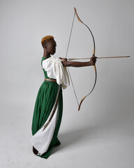 Full length portrait of pretty African woman wearing long green medieval fantasy gown holding bow...