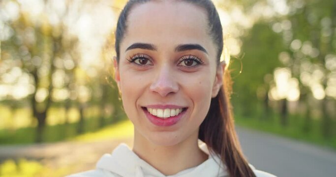 Close up shot of happy joyful Caucasian beautiful woman in good mood looking at camera and smiling standing on street in the morning. Young female with smile on face, outdoor workout, emotions concept