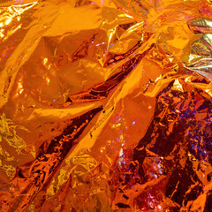 Holographic background. Real texture of iridescent film in bright orange colors.
