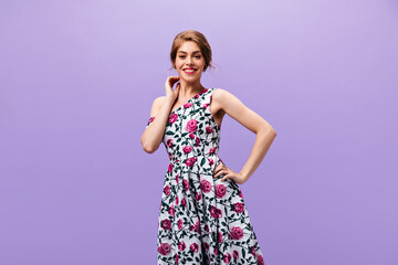 Positive lady in trendy dress smiles on purple background. Wonderful wavy haired woman in floral stylish clothes posing into camera..