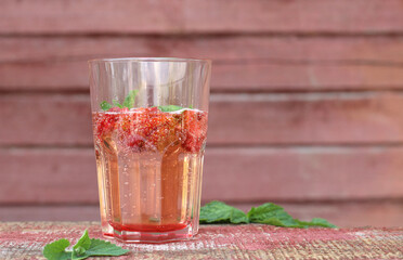 Lemonade with strawberries and mint in a glass on a pink background