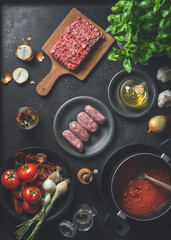 Various ingredients for  Sauce bolognese : Salsiccia sausages, minced meat, tomatoes sauce, herbs and spices on dark kitchen background. Top view. Cooking preparation
