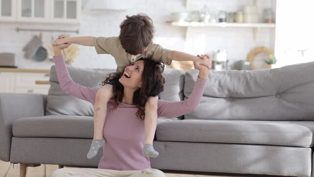 Carefree young mother or nanny carry preschool boy on shoulder have funny day at home. Cheerful loving mom enjoy active games playing with small son together on weekend. Parent and child bonding happy