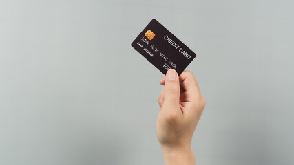 Hand is holding black credit card isolated on grey background.