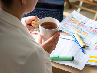 businesswoman holding a cup of coffee on a desk with paperwork, a laptop and highlights. Planning session with calendars for time management and productivity. Entrepreneur and remote work.