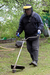 A man in a protective mask mowing the grass with a trimmer.