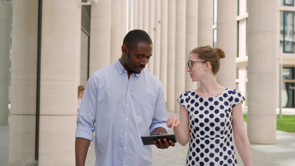 Obraz premium Young businessman using digital tablet and talking to colleague walking in city