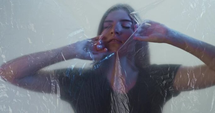 Against discrimination. Mind freedom. Removing social barriers. Sexism stereotypes. Anxious woman trying to breath behind clear plastic film in light defocused background.