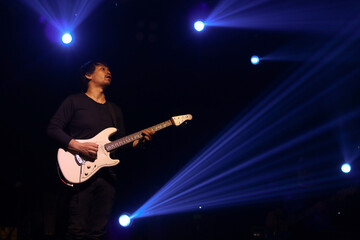 Obraz premium Guitar player in action on stage with colorful glow bright spotlights and smoke on rock stage concert in dark background, stage concert and music festival show concept.