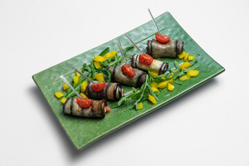close up of eggplant rolls with cream cheese on green plate on white background