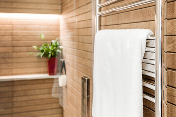 Wooden bathroom interior with heated towel rail and white towel on it - 445547571