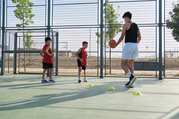 Basketball coach giving a basketball to a leg prosthesis student. Trainer training two kids.