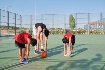 Basketball coach doing leg stretching exercises with two children, one of them has a leg prosthesis. Trainer training two kids.