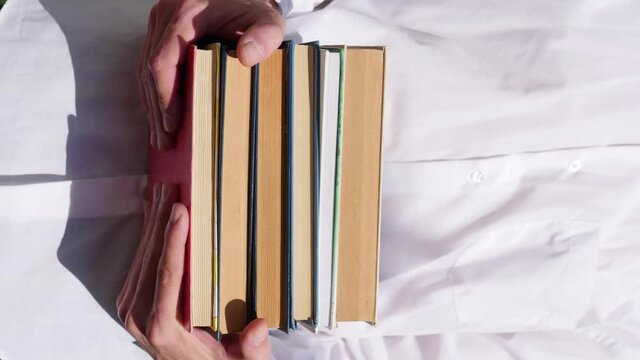 Man in white shirt holding stack of books. 4k vertical video. Education concept. Stop motion