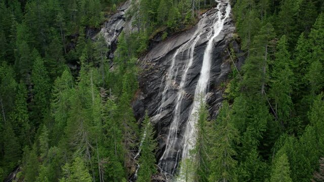 Aerial Reveal of Tall Waterfall Cliff in Dense Evergreen Forest