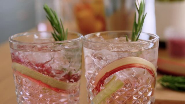 cold drinks and alcohol concept - glasses of rhubarb cocktails with rosemary at home