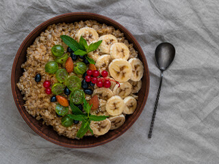 Wholegrain Oatmeal porridge bowl with fresh berries fruits nuts mint leaves flat lay. Healthy food oat meal morning breakfast top view. Whole grain cereal gooseberry currant banana on linen tablecloth