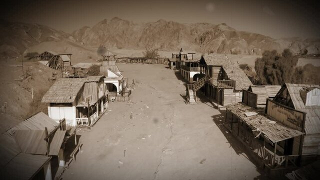 Wild west Town colored in old style Aerial view
Drone over Western town with desert mountains Old film look vignette and Sepia color 
